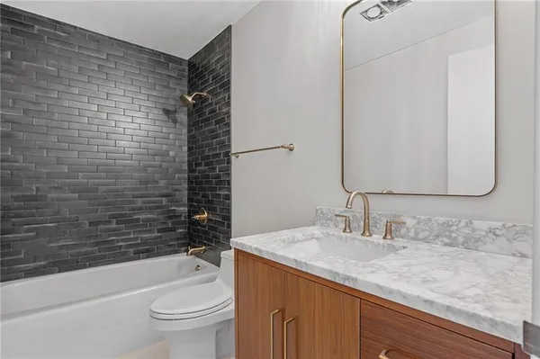 a bathroom with a granite countertop bathtub sink vanity mirror and toilet