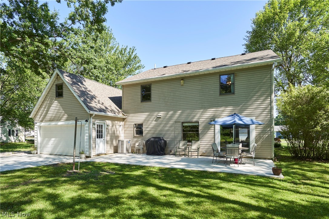 Rear view of property featuring a garage, a lawn, and a patio