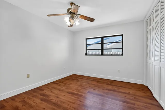 an empty room with wooden floor chandelier fan and windows