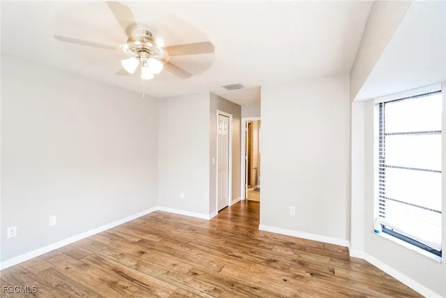 an empty room with wooden floor fan and windows