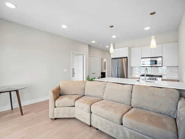 a living room with stainless steel appliances kitchen island a couch and a dining table with wooden floor