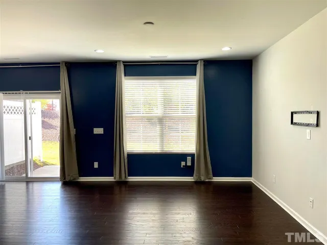 an empty room with wooden floor and windows with curtains