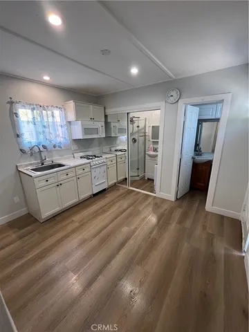 a kitchen with stainless steel appliances granite countertop a refrigerator a sink dishwasher a stove and white countertops with wooden floor