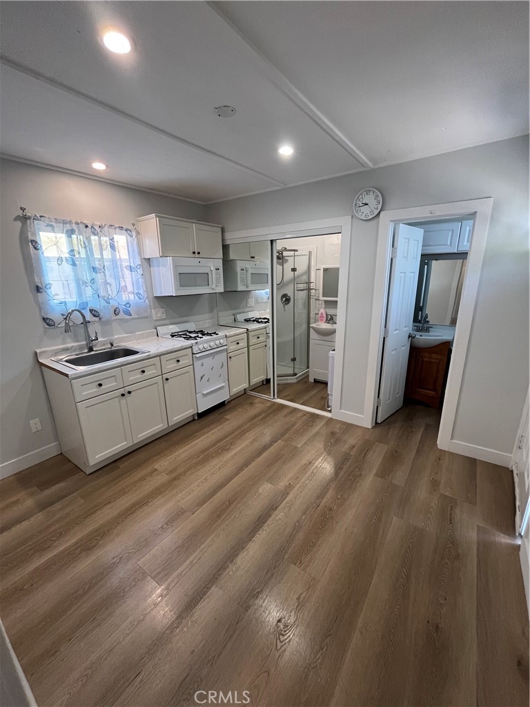 a kitchen with stainless steel appliances granite countertop a refrigerator a sink dishwasher a stove and white countertops with wooden floor