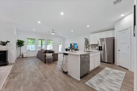 a open kitchen with stainless steel appliances granite countertop a stove top oven a refrigerator a sink and a dining table with wooden floor