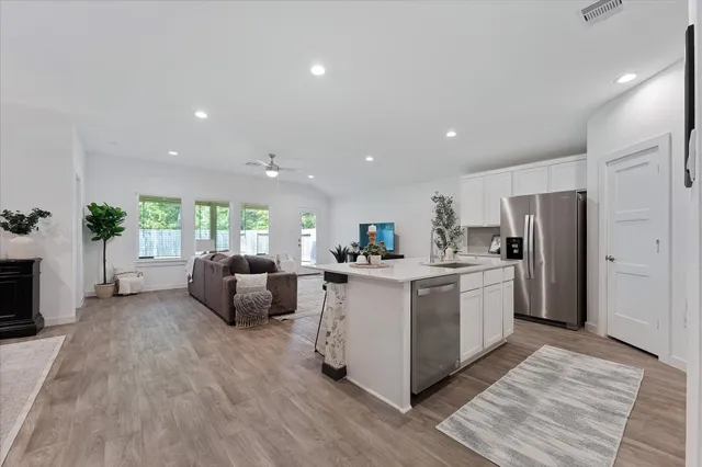 a open kitchen with stainless steel appliances granite countertop a stove top oven a refrigerator a sink and a dining table with wooden floor