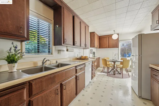 a kitchen with stainless steel appliances granite countertop a refrigerator a sink dishwasher a dining table and chairs with wooden floor