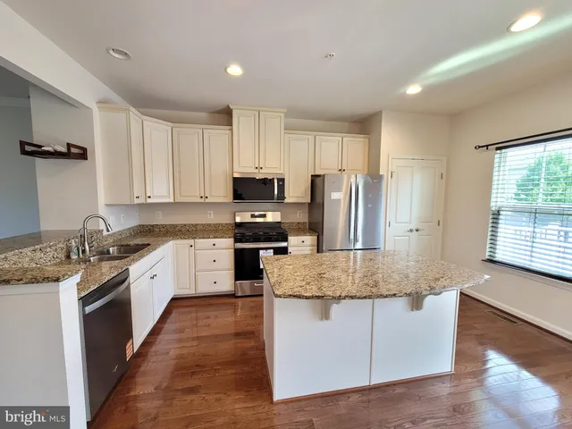 a large kitchen with granite countertop a stove top oven a sink dishwasher a refrigerator and white cabinets with wooden floor