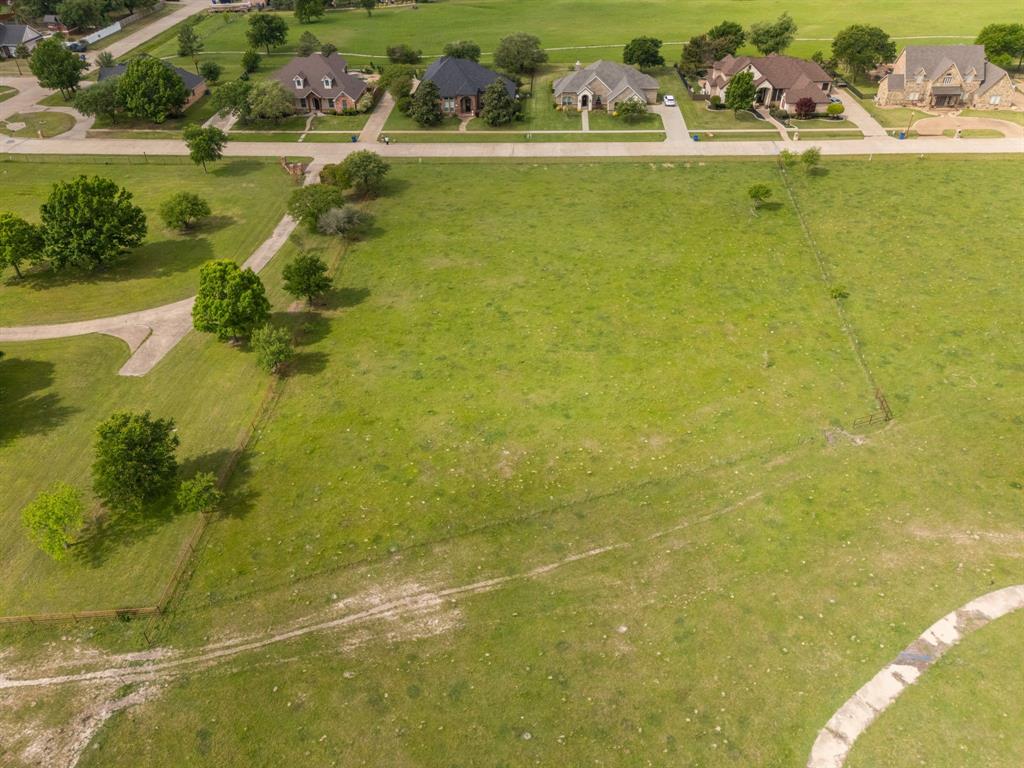 Tbd Sleepy Hollow Road Ennis, TX 75119 - Photo 10 of 11 An expansive green field with a partial paved road and trees, offering views of residential properties in the background