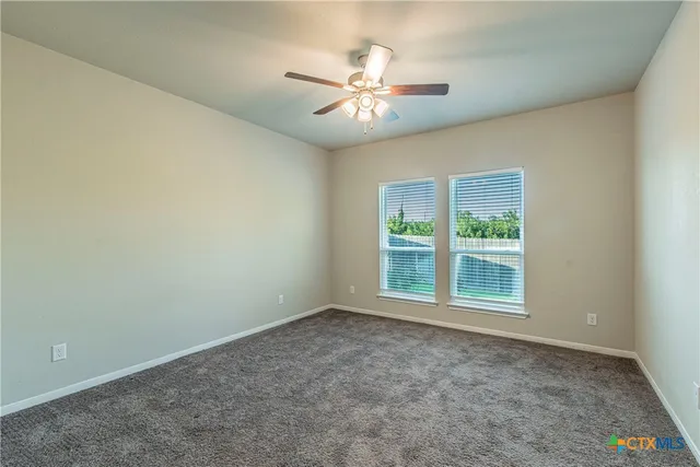 an empty room with a chandelier fan and windows