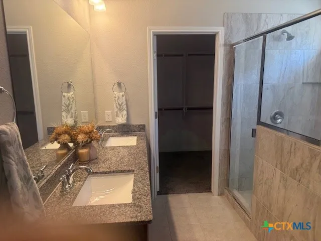 a bathroom with a granite countertop double vanity sink a mirror and a shower