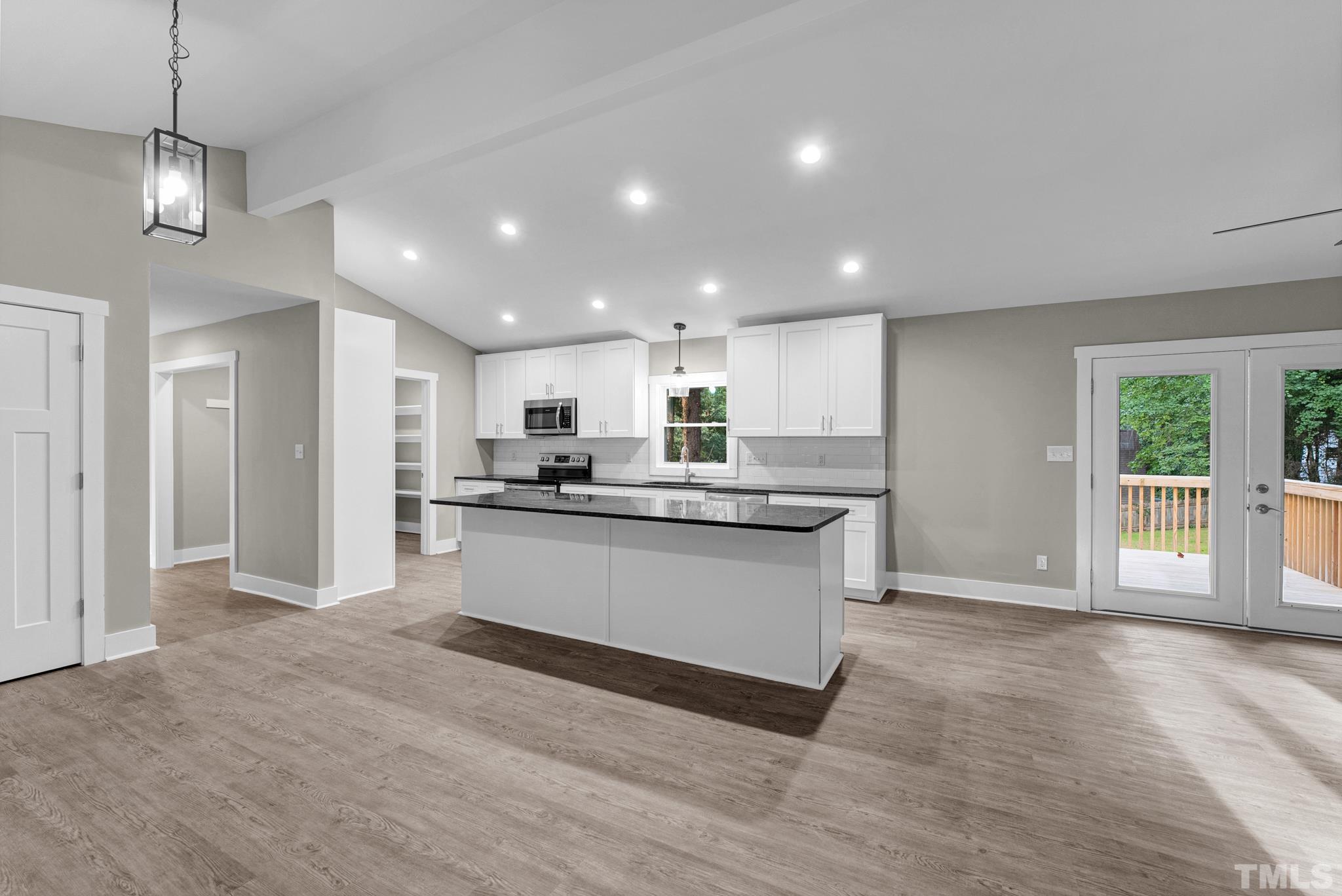 6712 Millbridge Court Raleigh, NC 27615 - Photo 5 of 25 a large white kitchen with kitchen island a sink wooden floor and a refrigerator
