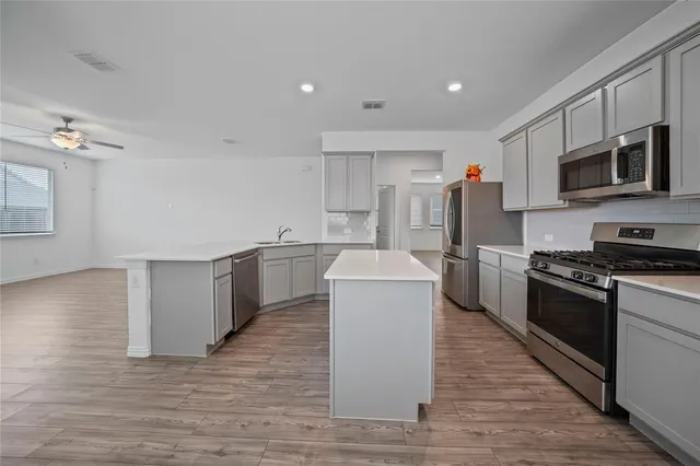 a kitchen with stainless steel appliances a stove top oven a sink a refrigerator white cabinets and wooden floor