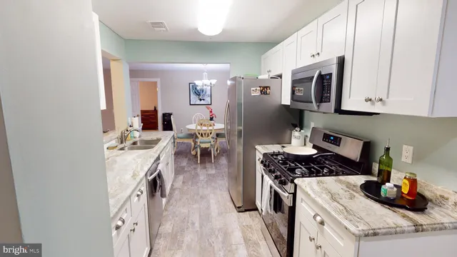 a kitchen with stainless steel appliances granite countertop a stove a sink a refrigerator and white cabinets with wooden floor