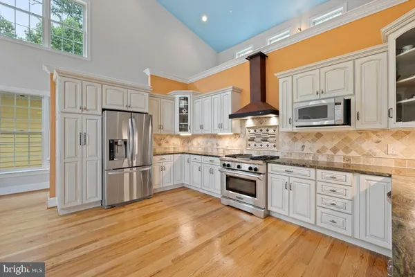 a kitchen with stainless steel appliances granite countertop a stove top oven a refrigerator and white cabinets with wooden floors