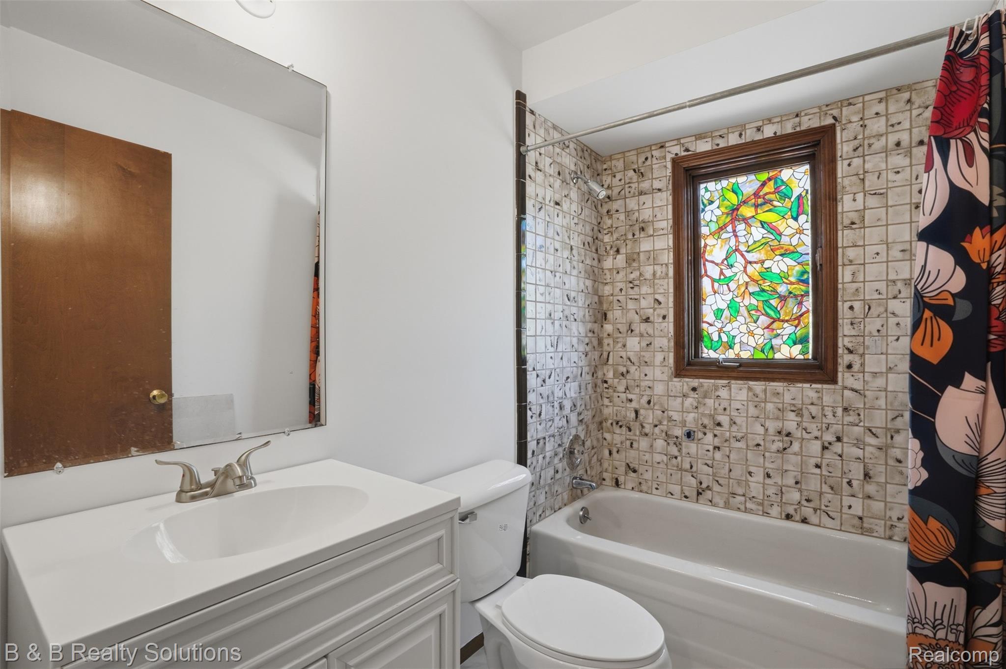 780 North Van Dyke Road, Unit APARTMENT #1 Almont, MI 48003 - Photo 25 of 28 Bathroom featuring a stained glass window, white vanity with integrated sink, chrome faucet, tiled shower surround, and a white bathtub