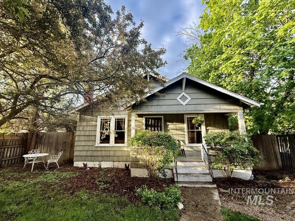 Charming bungalow featuring a covered front porch with white columns, light green siding, and a diamond-shaped accent on the front gable