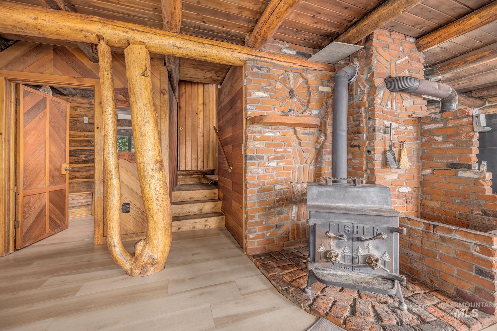 2150 Seid Creek Road Cambridge, ID 83610 - Photo 11 of 50 Interior space featuring a wood-burning stove with brick surround and hearth, exposed wood beam ceiling, wood-finish flooring, and wooden staircase