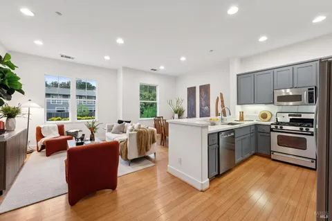 a kitchen with stainless steel appliances granite countertop a stove top oven a sink dishwasher a dining table and chairs with wooden floor