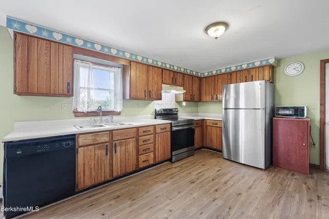 a kitchen with granite countertop wooden floors stainless steel appliances a sink and a window