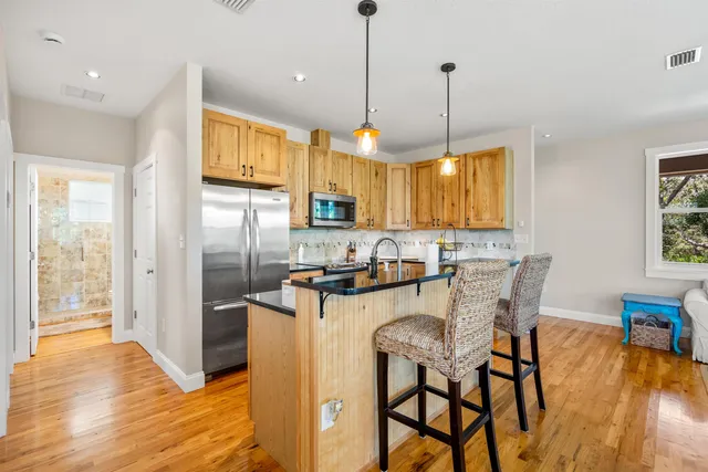 a kitchen with stainless steel appliances granite countertop a stove top oven a refrigerator a sink and a dining table with wooden floor