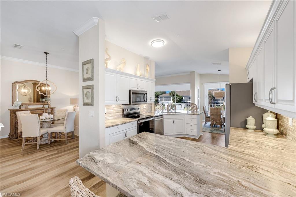 6879 Redbay Park Road, Unit 203 Naples, FL 34109 - Photo 16 of 43 Kitchen with a chandelier, ornamental molding, stainless steel appliances, white cabinetry, and light wood finished floors