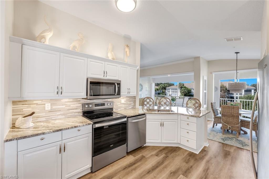 6879 Redbay Park Road, Unit 203 Naples, FL 34109 - Photo 17 of 43 Kitchen with stainless steel appliances, a peninsula, light stone counters, white cabinets, and decorative light fixtures