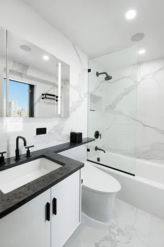 a bathroom with a granite countertop sink a toilet a mirror and bathtub