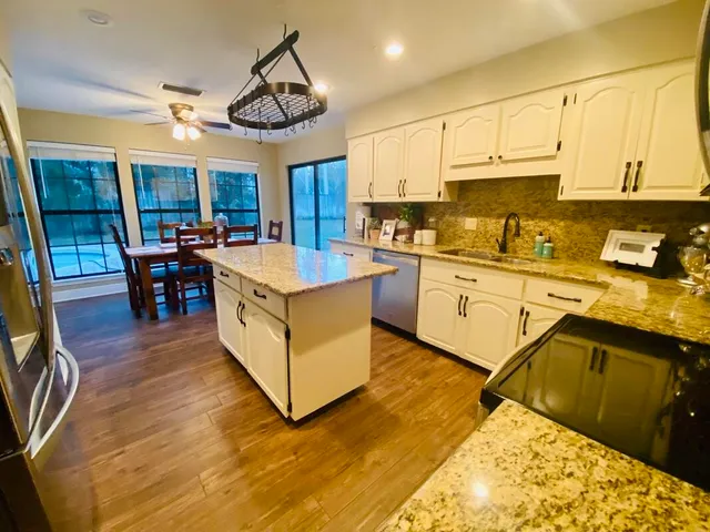 a open kitchen with stainless steel appliances granite countertop a stove top oven a sink dishwasher and white cabinets with wooden floor