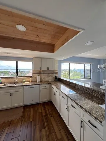 a large kitchen with granite countertop a stove a sink and white cabinets with wooden floor