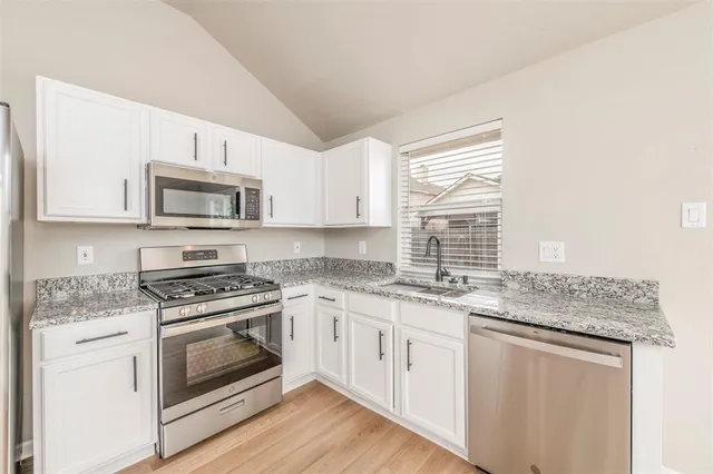 a kitchen with stainless steel appliances granite countertop a stove a sink and white cabinets