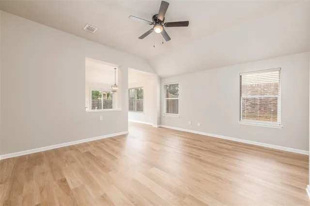 an empty room with wooden floor ceiling fan and windows