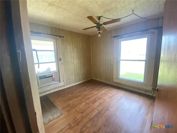 an empty room with wooden floor fan and windows