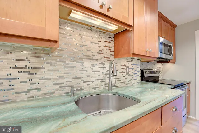 a open kitchen with kitchen island granite countertop wooden cabinets a sink a window and stainless steel appliances