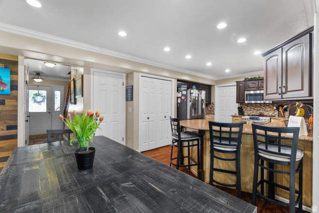 5727 South 3550th Street West Roy, UT 84067 - Photo 20 of 49 Open-concept living space featuring recessed lighting, crown molding, a kitchen peninsula with granite countertops, a tile backsplash, and hardwood flooring