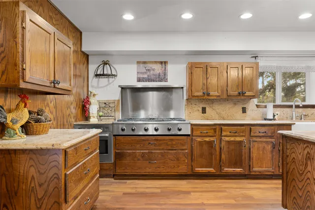 a kitchen with stainless steel appliances granite countertop a stove top oven a sink dishwasher a dining table and chairs with wooden floor