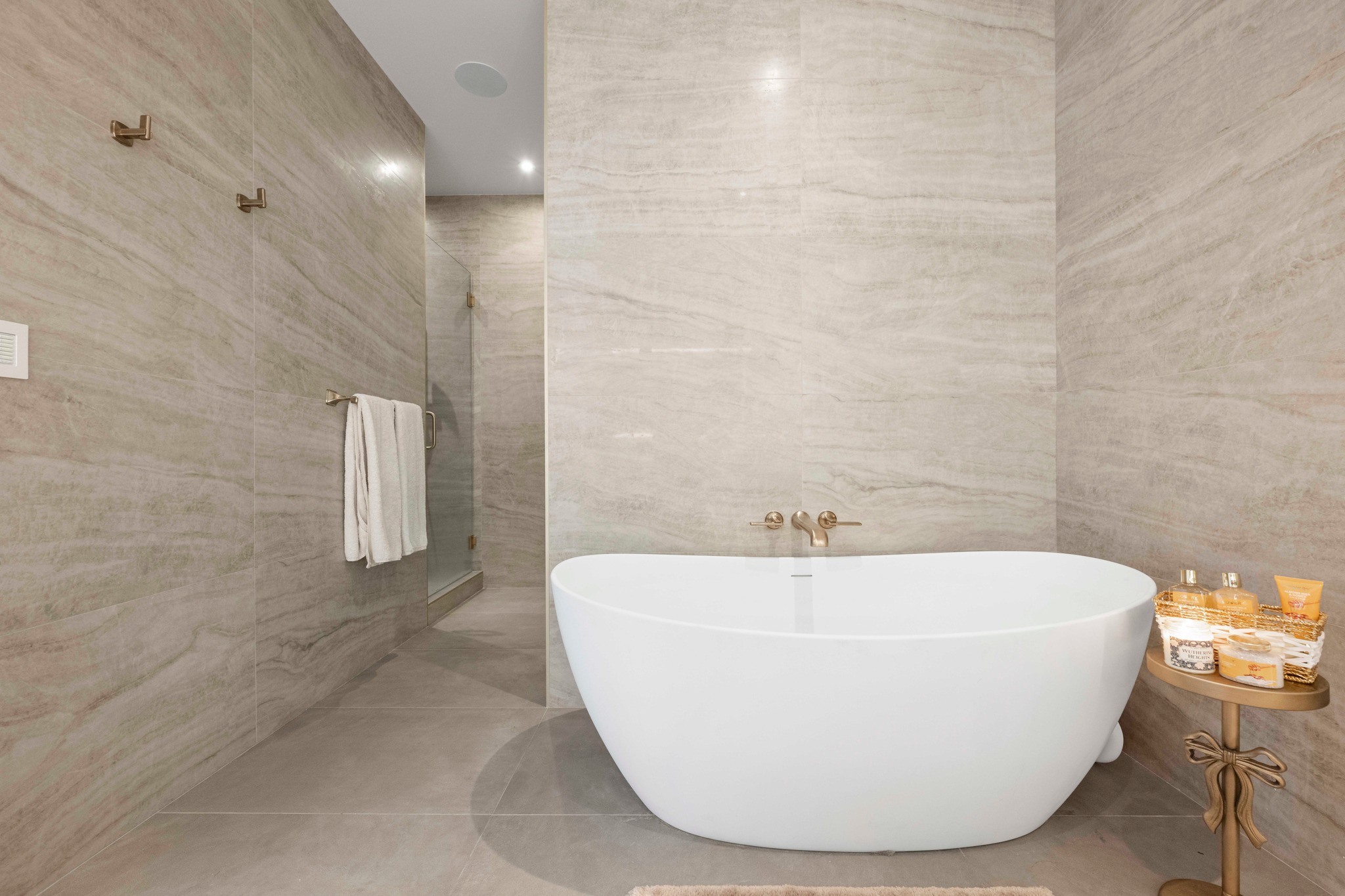 210 Lavaca Street, Unit 2706 Austin, TX 78701 - Photo 12 of 32 Freestanding soaking tub with wall-mounted brass fixtures, complemented by full-height stone-look tile walls and a glass-enclosed shower