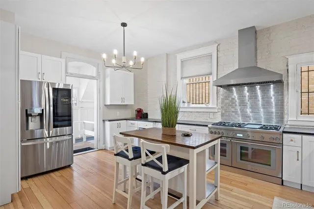 a kitchen with stainless steel appliances granite countertop a stove a refrigerator a kitchen island a stove a dining table and chairs with wooden floor