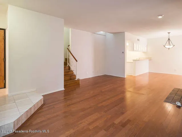 a view of empty room with wooden floor and kitchen
