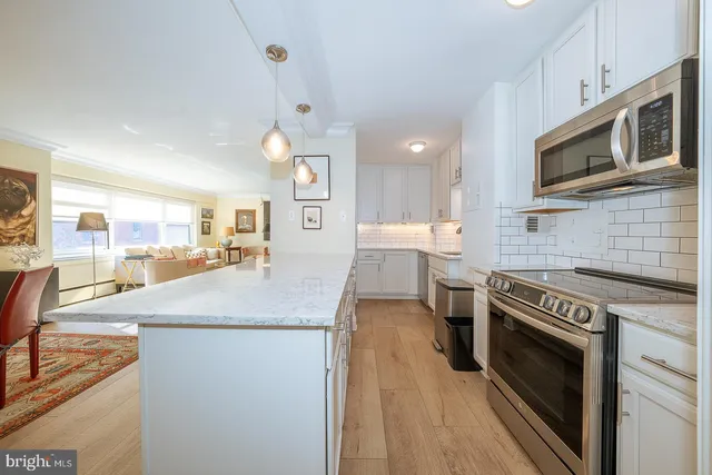 a kitchen with stainless steel appliances kitchen island granite countertop a stove top oven a sink dishwasher and white cabinets with wooden floor