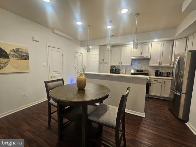 a kitchen with stainless steel appliances granite countertop a dining table chairs refrigerator and sink