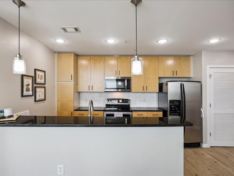 5925 Almeda Road, Unit 12202 Houston, TX 77004 - Photo 2 of 33 Contemporary kitchen featuring sleek maple cabinetry, granite countertops, stainless steel appliances, abundant storage, and a spacious breakfast bar—perfect for entertaining or everyday living.