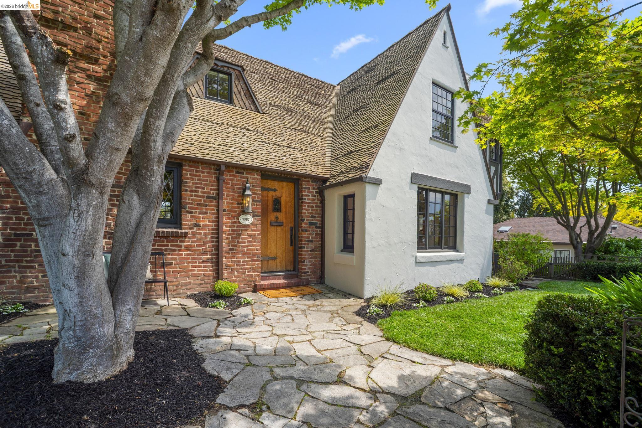 1087 Hubert Road Oakland, CA 94610 - Photo 58 of 67 Charming facade featuring a natural wood entry door, brick and stucco exterior, stone pathway, and manicured landscaping