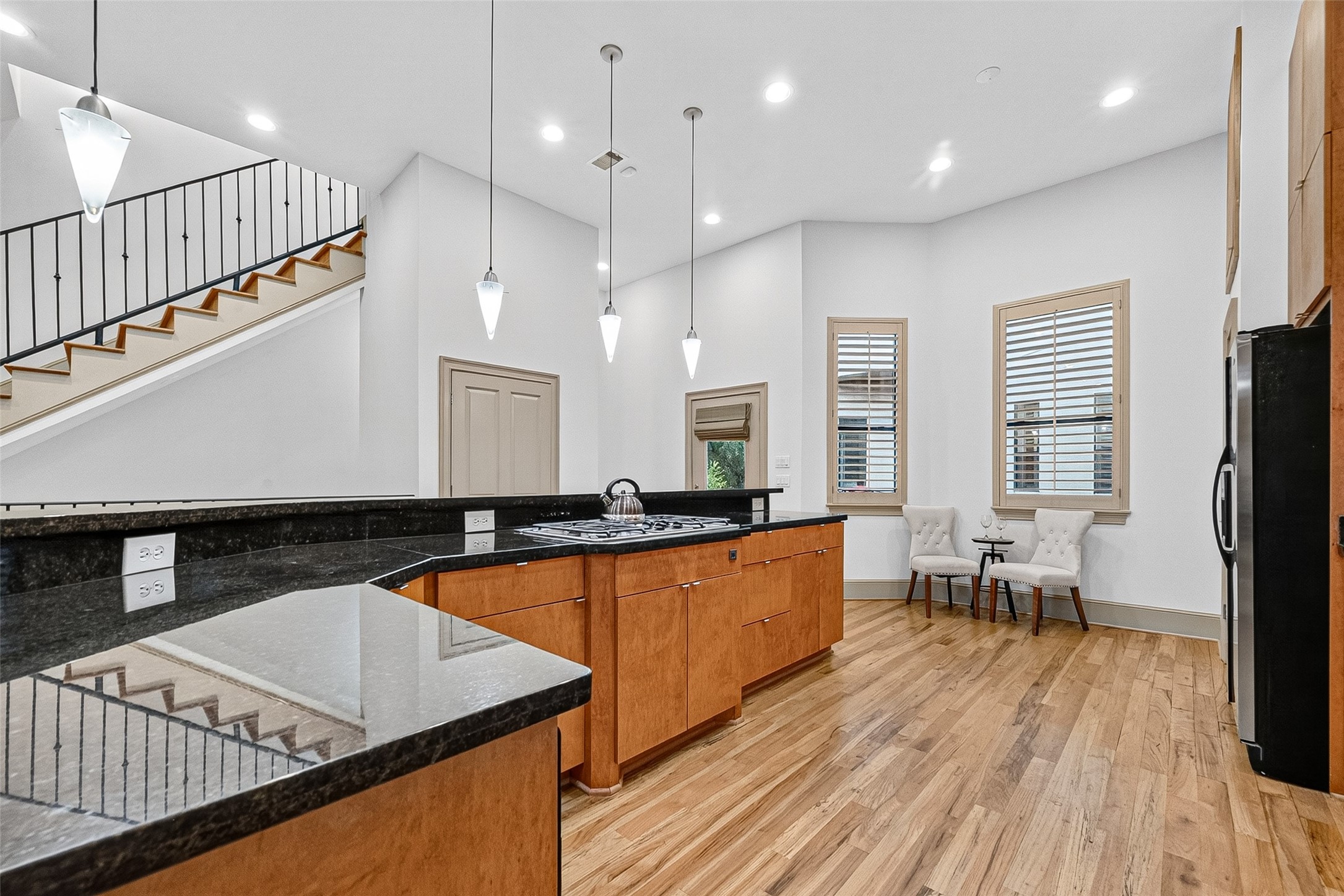 2034 Colquitt Street, Unit A Houston, TX 77098 - Photo 15 of 41 This bright kitchen features modern pendant lighting, granite countertops, and warm wood cabinetry. The open layout includes a breakfast nook with two chairs and a table, hardwood floors, and a view of a staircase with sleek black railings.