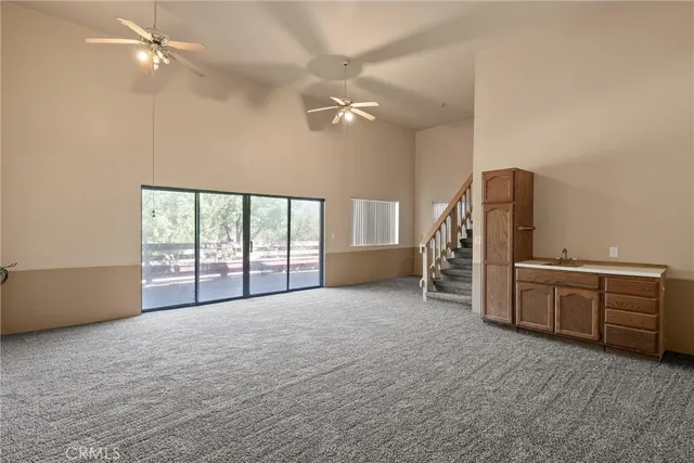 an empty room with chandelier fan and windows