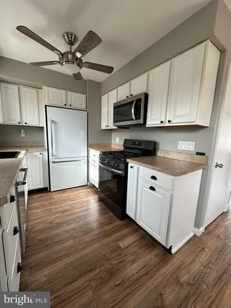 a kitchen with stainless steel appliances granite countertop a refrigerator a stove a sink and white cabinets with wooden floor