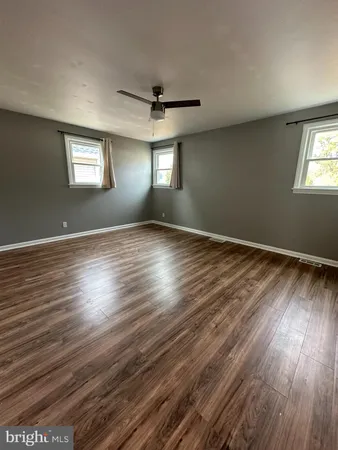 an empty room with wooden floor ceiling fan and windows