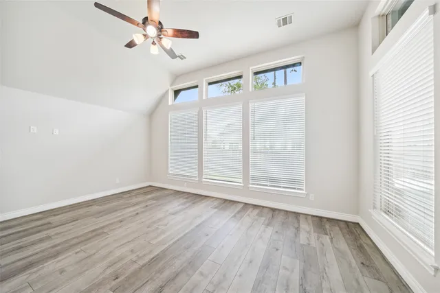 an empty room with wooden floor chandelier fan and windows