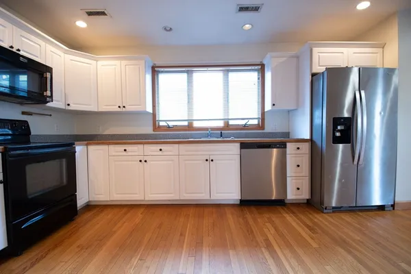 a kitchen with granite countertop a refrigerator a sink a stove a microwave and wooden floors