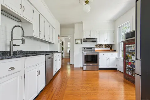 a kitchen with stainless steel appliances granite countertop a stove top oven a sink dishwasher and white cabinets with wooden floor